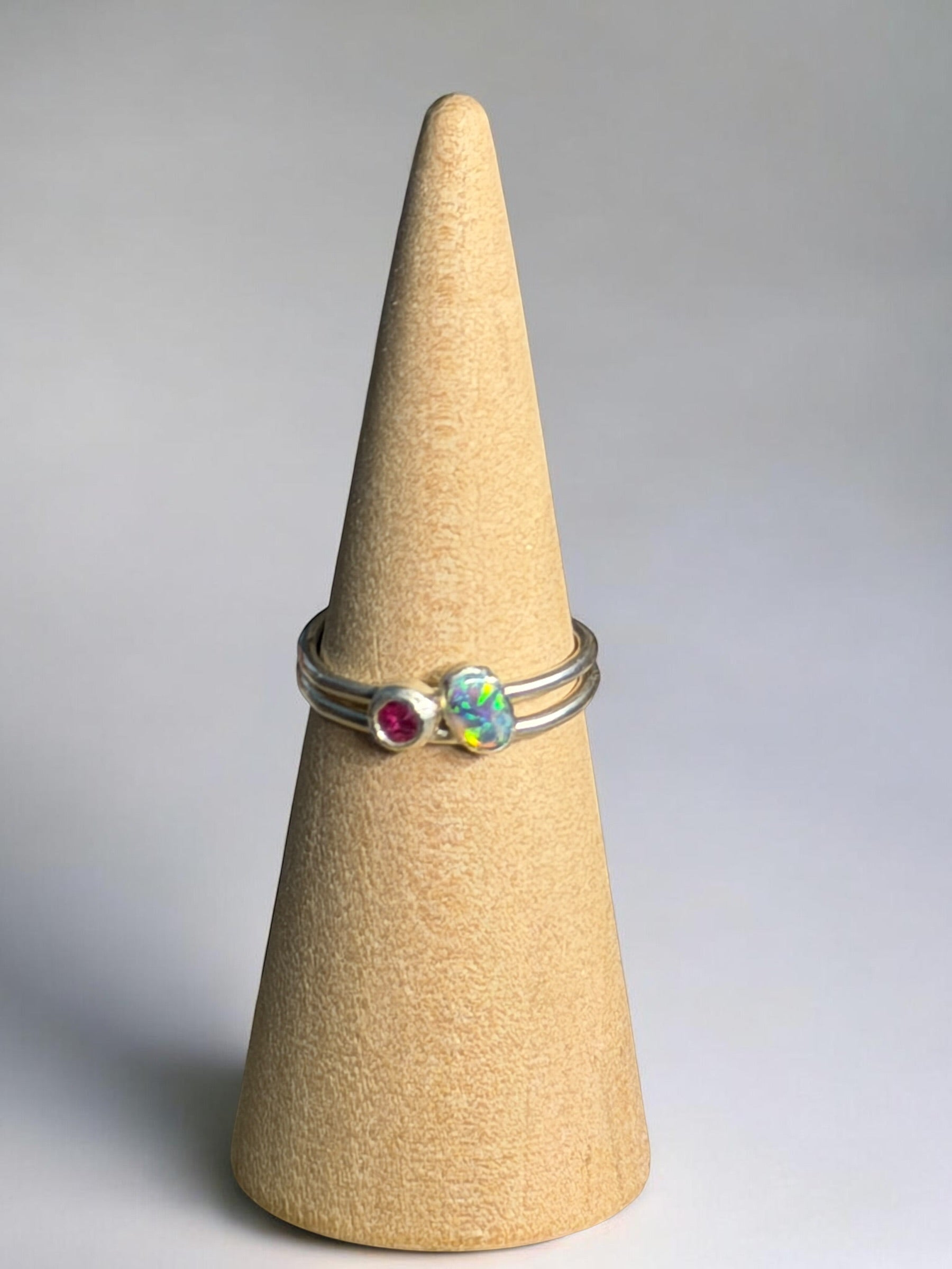 Gemstone silver ring with Australian opal and natural red ruby on a beige cone against a grey background