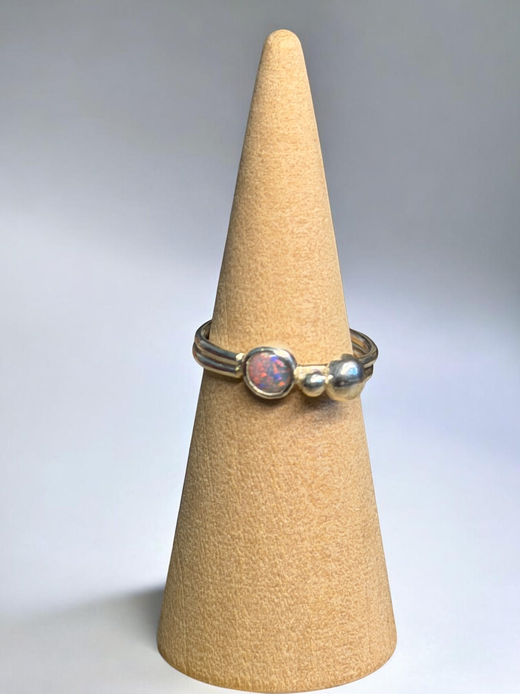 Ring with a pink stone on a beige cone-shaped stand against a gray background