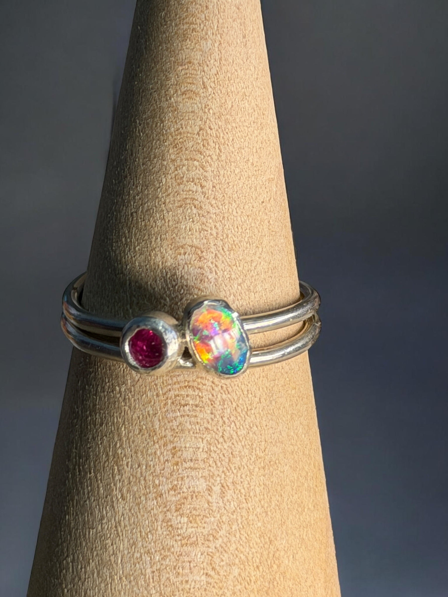 Silver ring with gemstones on a wooden stand against a dark background

Details