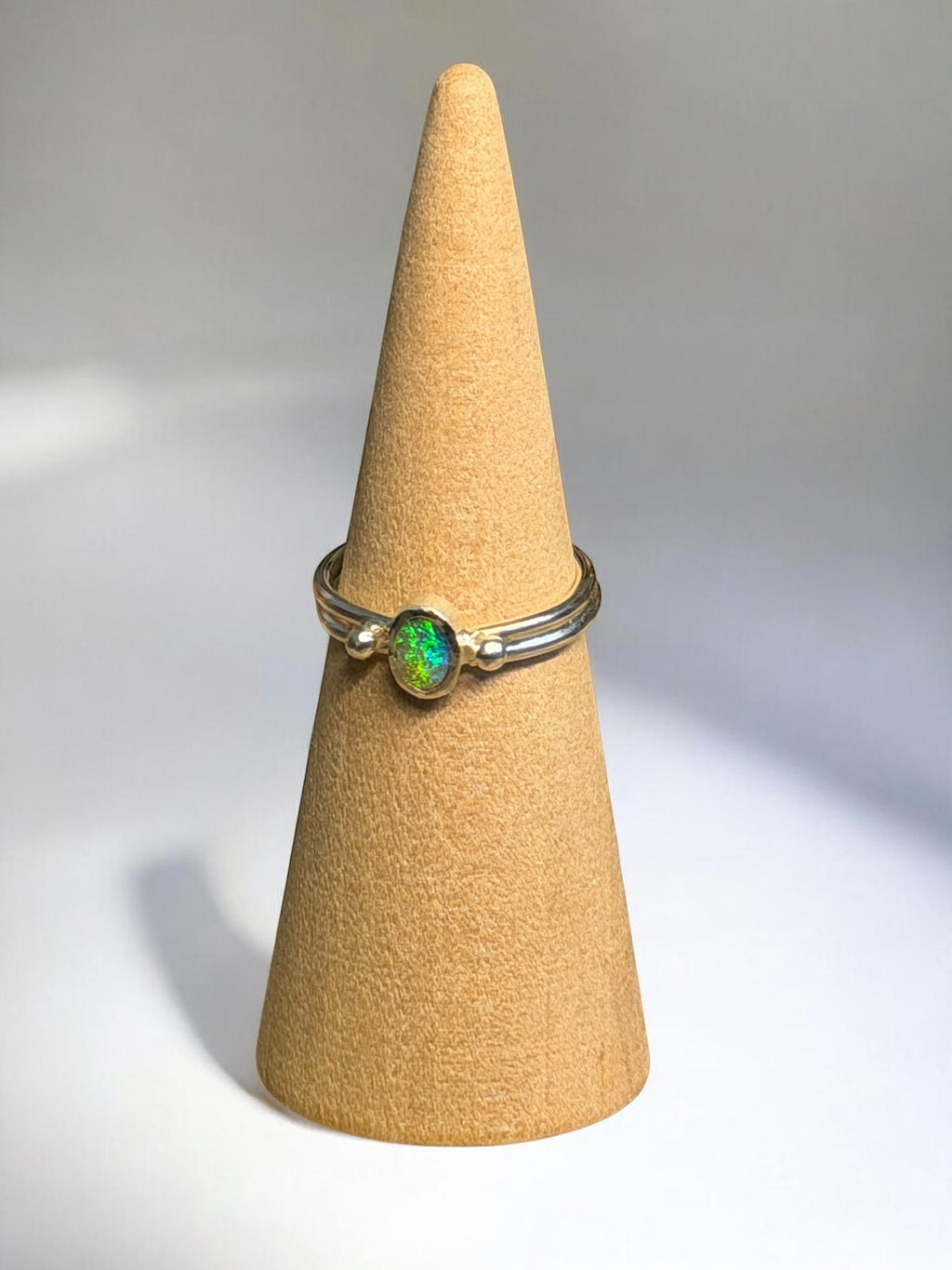 Ring with a green gemstone on a beige cone-shaped stand against a gray background