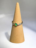 Ring with a green gemstone on a beige cone-shaped stand against a gray background