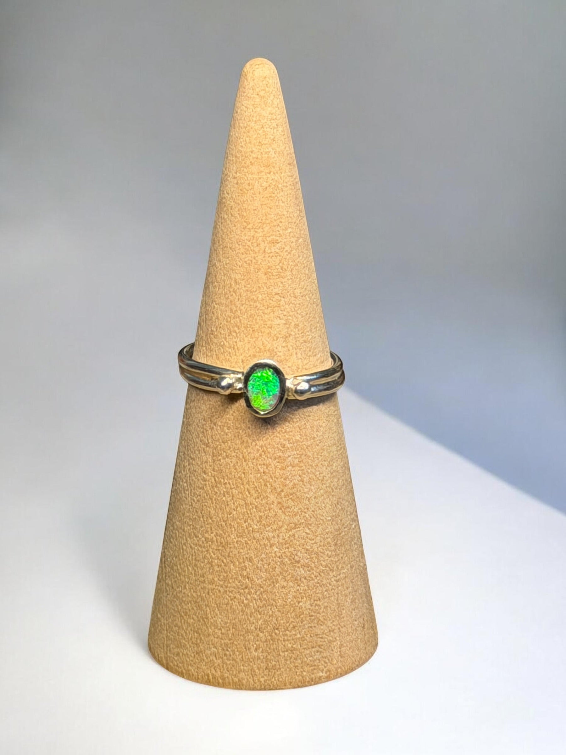 Gold ring with a green gemstone on a beige cone-shaped stand against a gray background