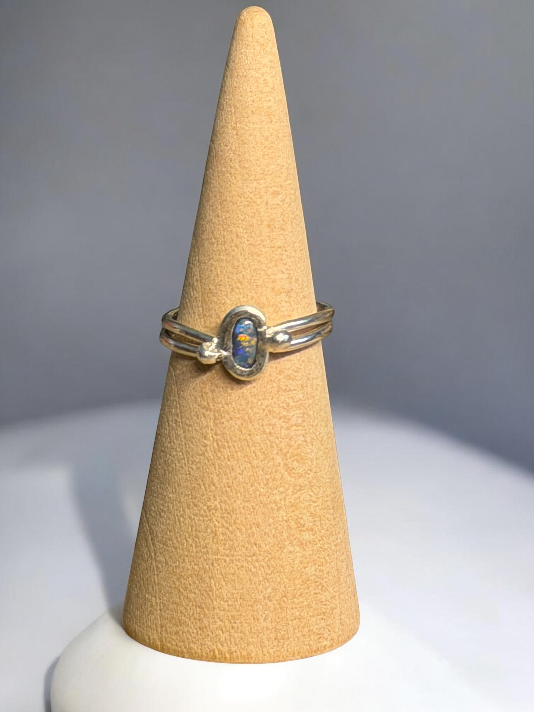 Silver ring with blue stone on a beige cone-shaped stand against a gray background