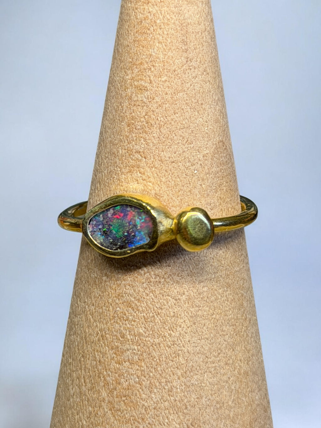 Gold ring with a colorful stone on a beige ring stand against a light gray background