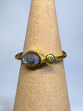 Gold ring with a colorful stone on a beige ring stand against a light gray background