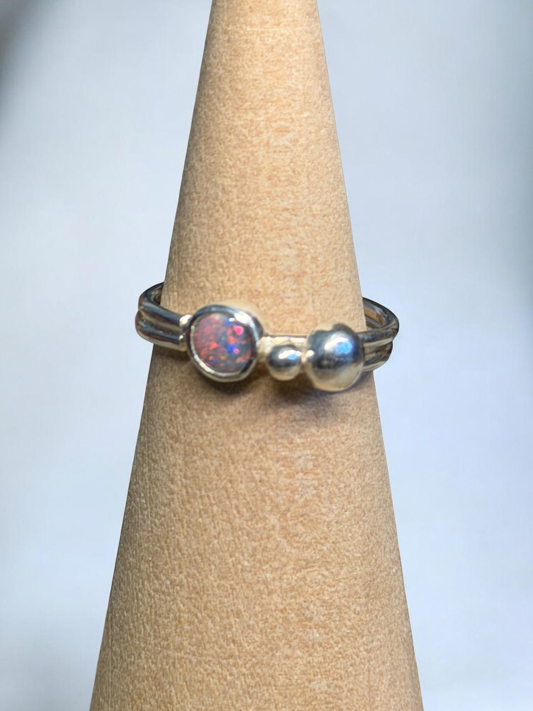 Silver ring with a central opal stone on a beige ring stand against a light gray background