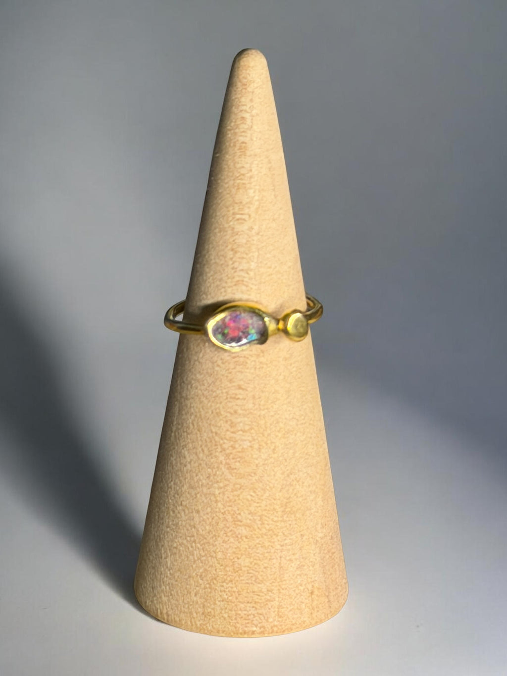 Gold ring with a colorful gemstone on a beige cone against a gray background