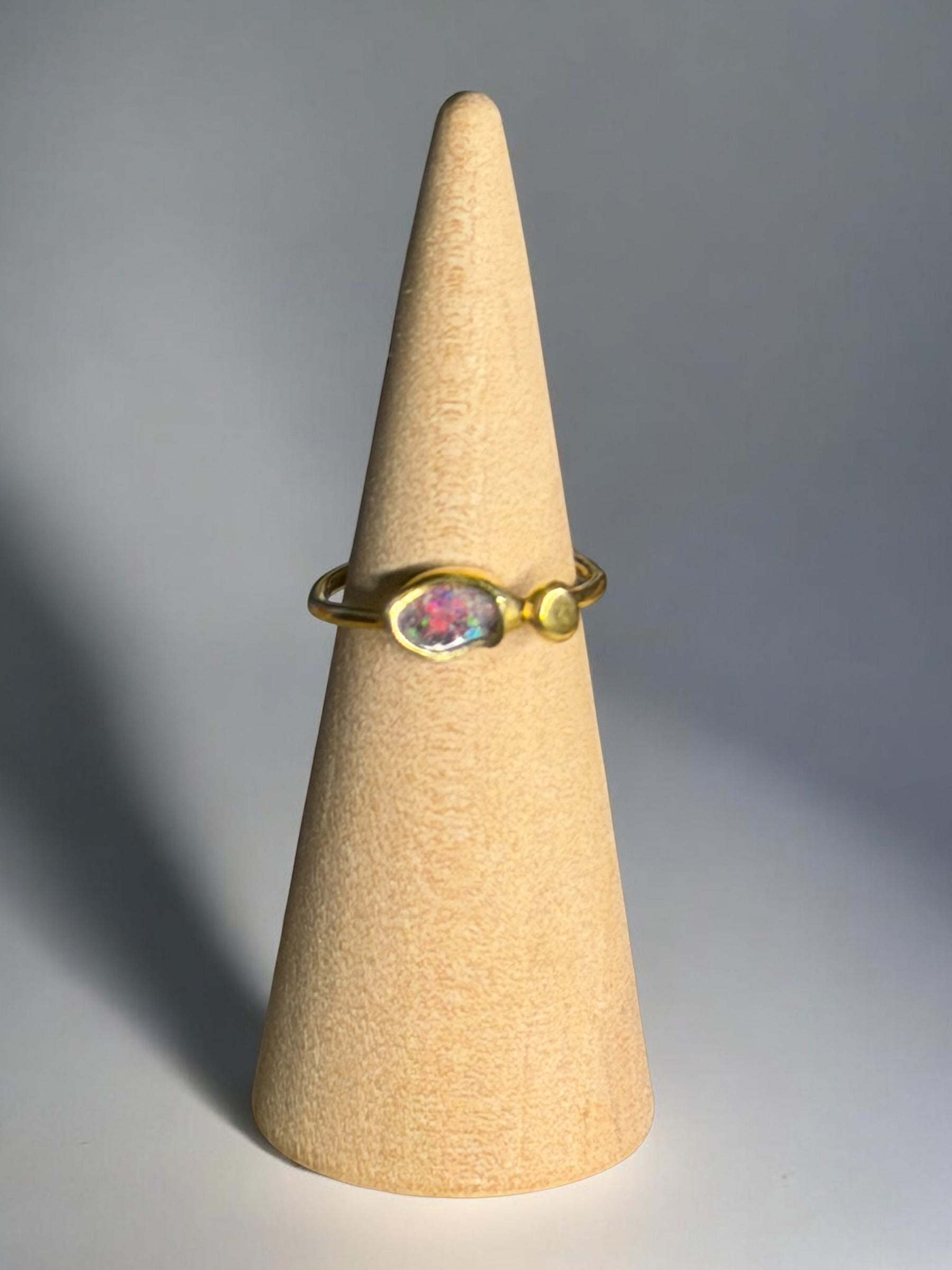 Gold ring with a colorful gemstone on a beige cone against a gray background
