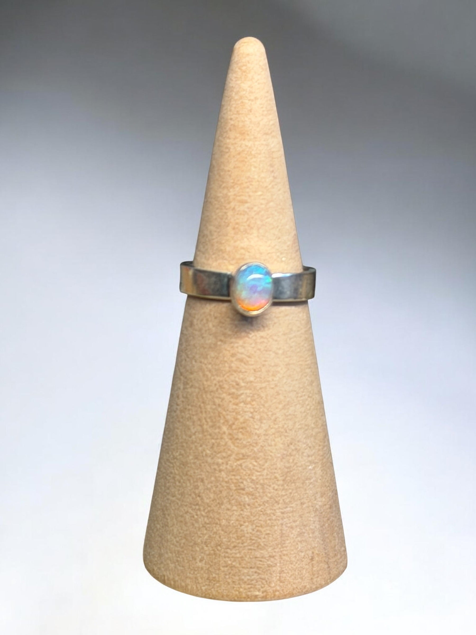 Ring with a colorful stone on a beige cone-shaped stand against a gray background