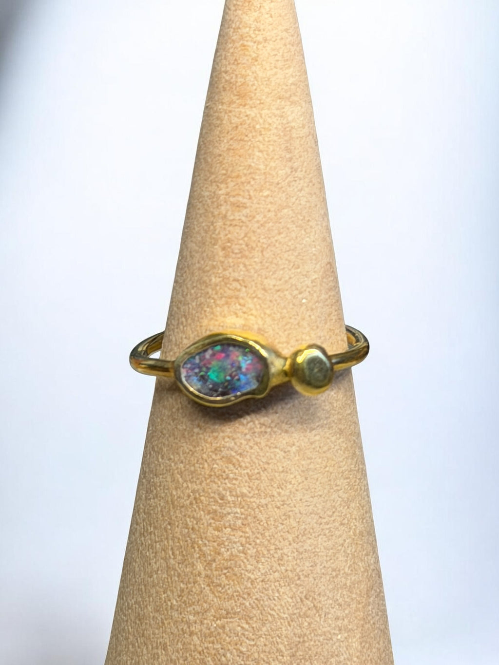 Gold ring with an opal stone on a beige cylindrical stand against a light background